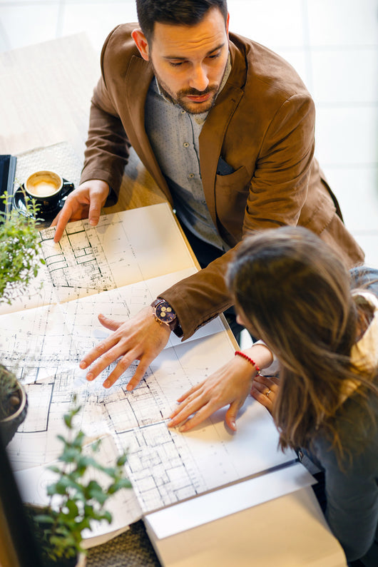 Man and woman both with dark hair, look over architectural plans.