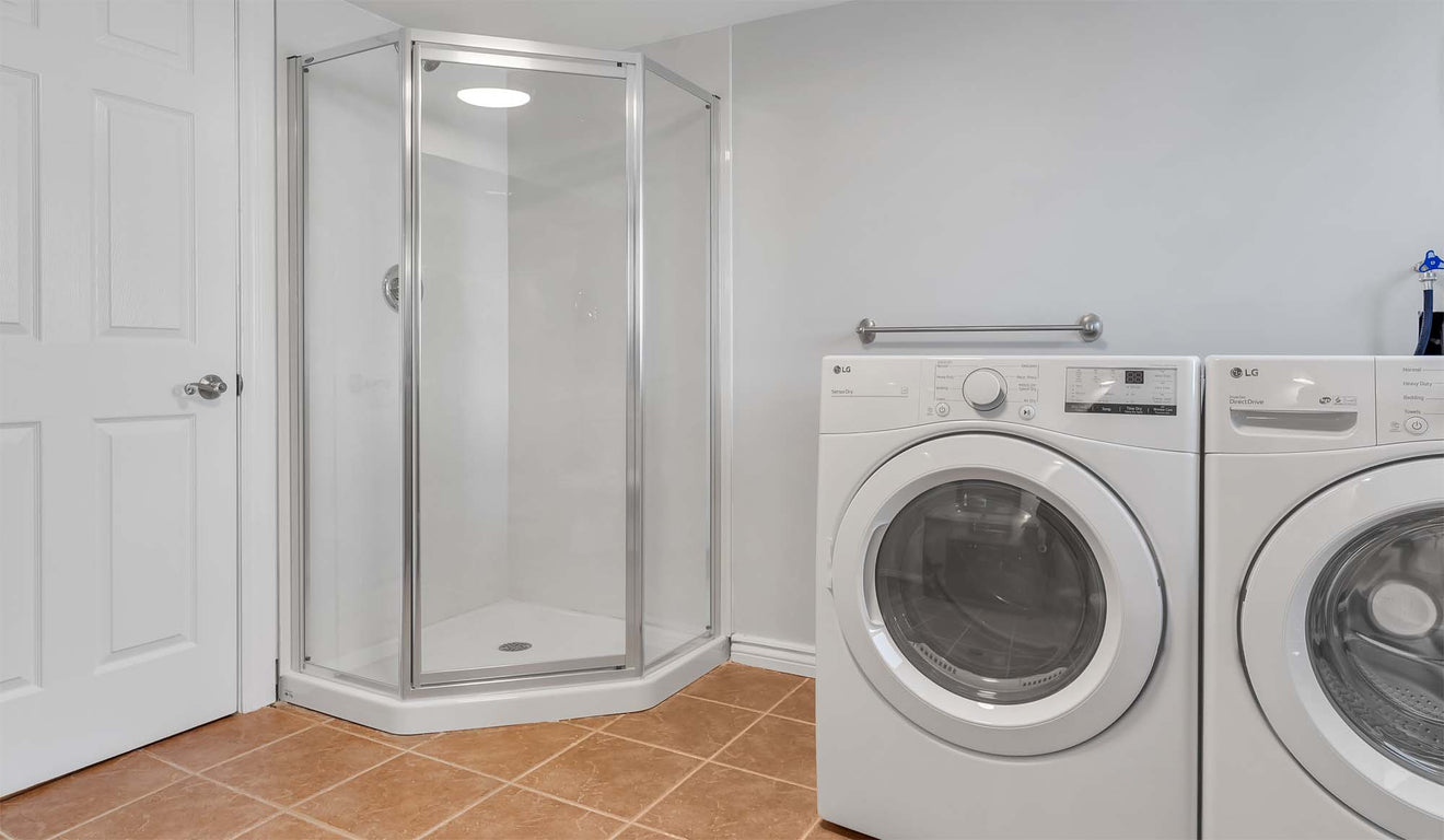 A glass shower on the left, next to a washer and dryer set-up.